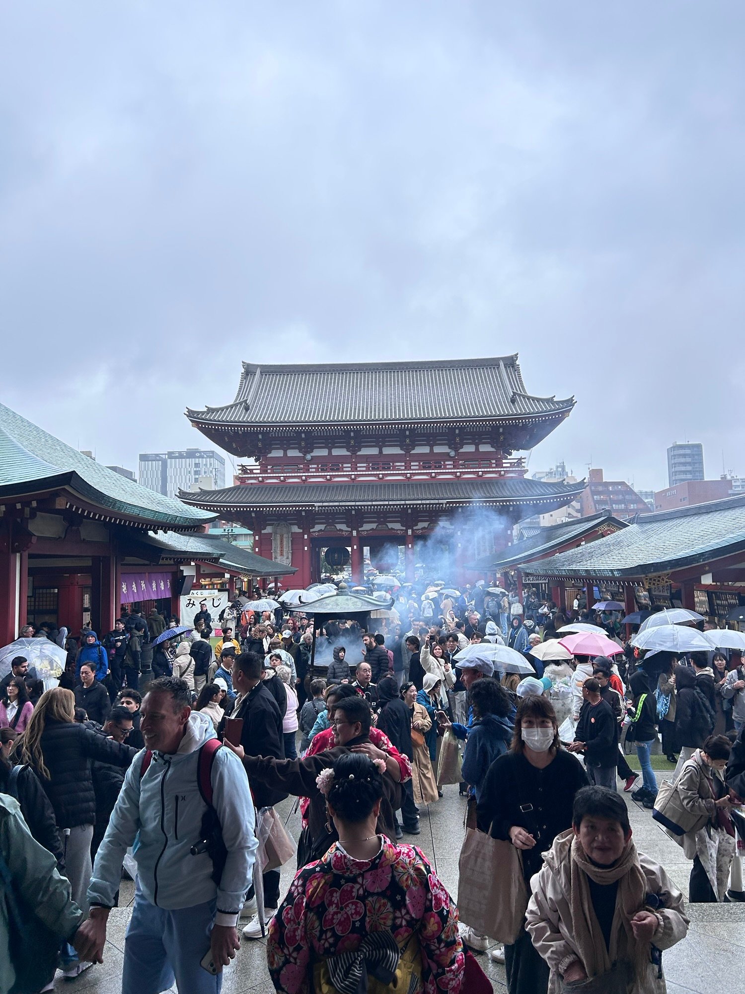 Gneča pred templjem Senso-ji v Asakusi v deževnem dnevu, tradicionalna arhitektura in obiskovalci s pisanimi dežniki.